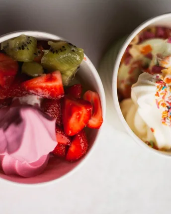 Two cups of frozen yogurt topped with sliced strawberries, kiwi and sprinkles.