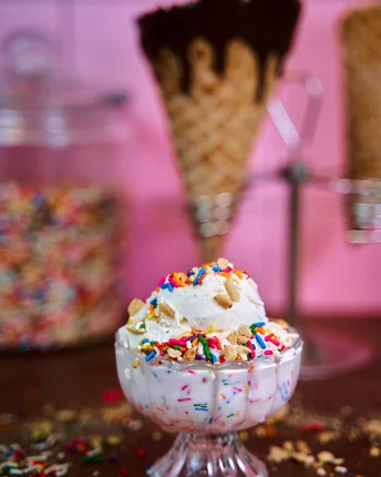 A frozen yogurt sundae in a glass dish with sprinkles and chopped nuts.