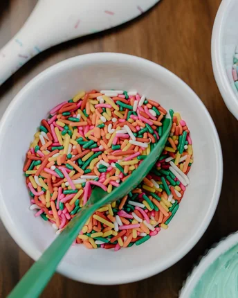 Bowls of coloured sprinkles with a scoop, on a wooden counter.